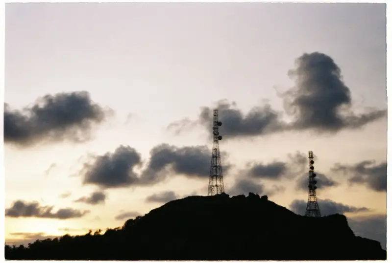 Transmission towers silhouetted on a hilltop against a cloudy sunrise