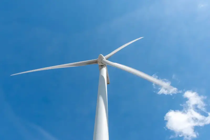 Single wind turbine with long blades against a bright blue sky