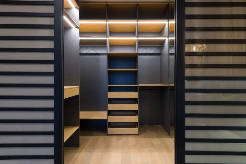 Dark closet system with LED-lit shelves, drawers and wood floor behind slatted doors