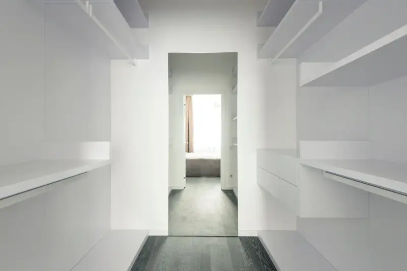 Empty white walk-in closet with shelves and hanging rods on both sides