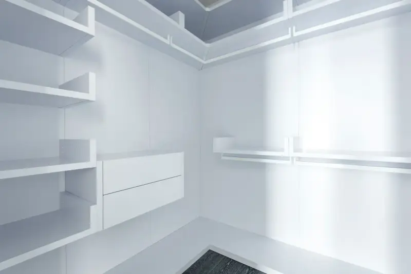 Corner of a white closet with floating shelves and a drawer unit