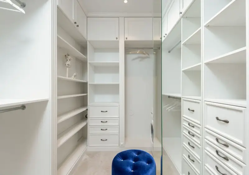 Built-in white wardrobe with shaker drawers, open shelves and a blue pouf