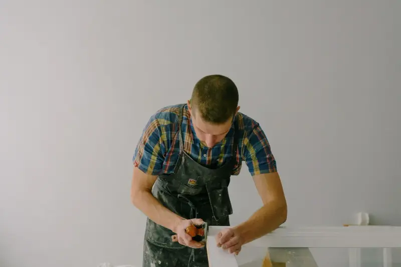 Joiner in an apron working on a white panel in a bright room