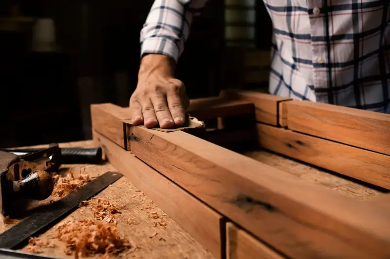 Woodworker sanding a wooden frame by hand on a bench covered in shavings