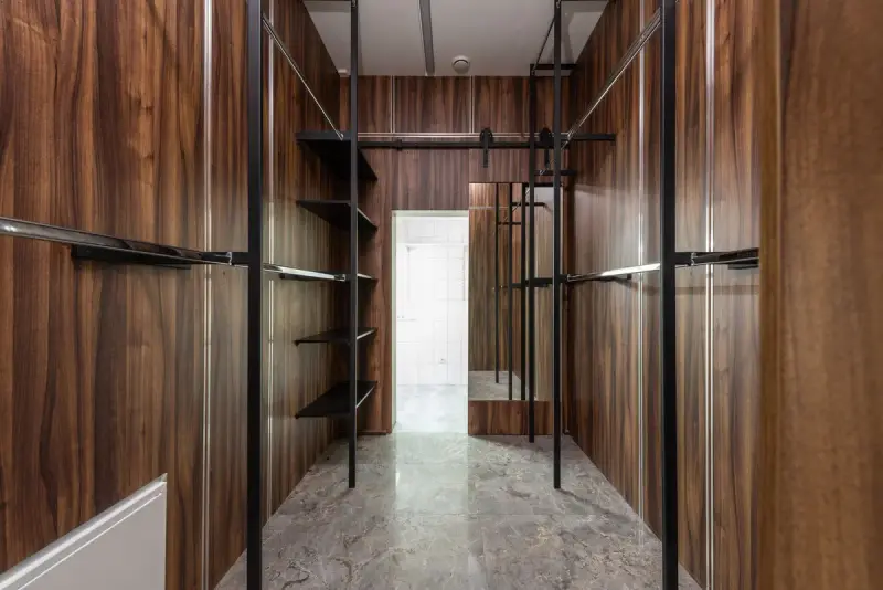 Walk-in closet with walnut panels, black metal rods and a marble floor