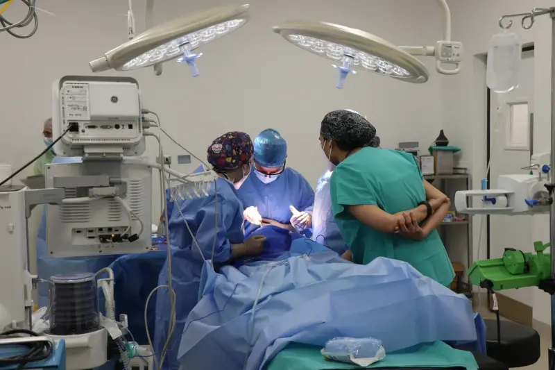 Surgical team of three women operating under two bright LED lights beside monitoring equipment