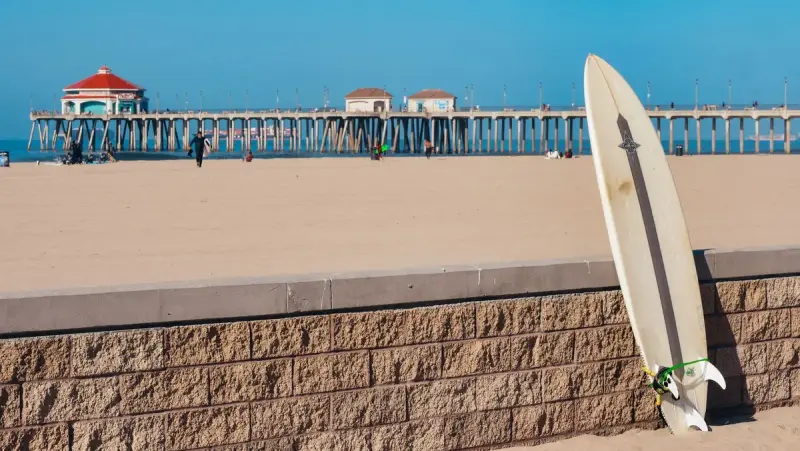 A surfboard leaning on a low brick wall with Huntington Beach Pier behind it