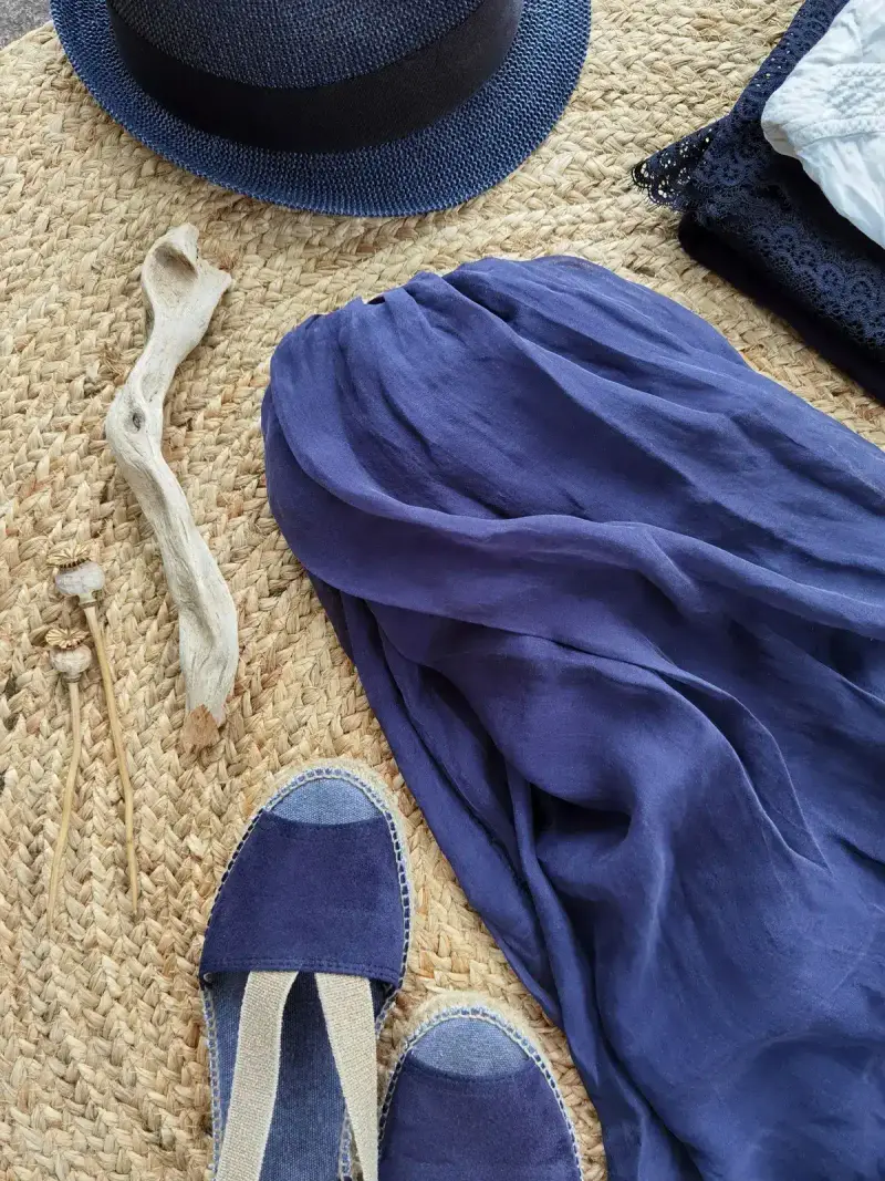 Resort flat lay of a navy straw hat, cobalt silk wrap and espadrilles on a jute rug