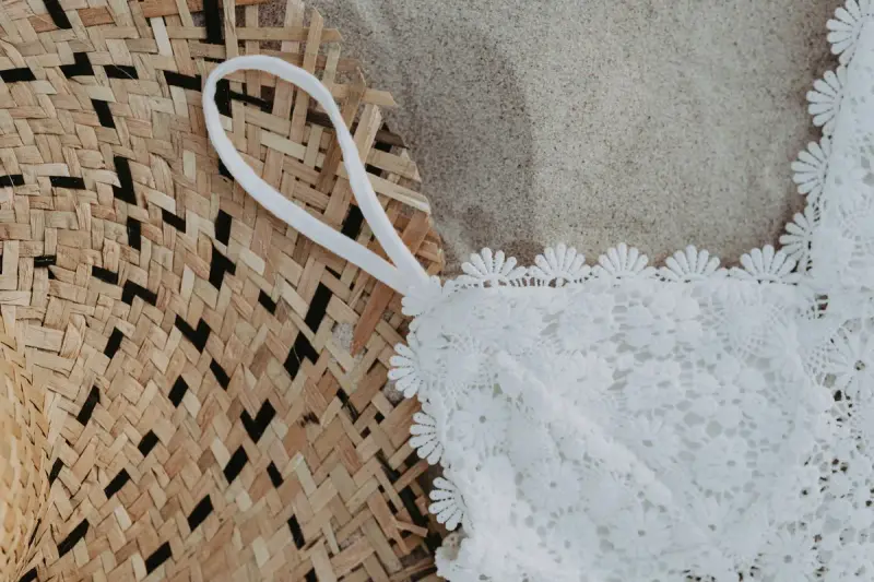 A lace swimsuit and a woven straw hat laid on beach sand