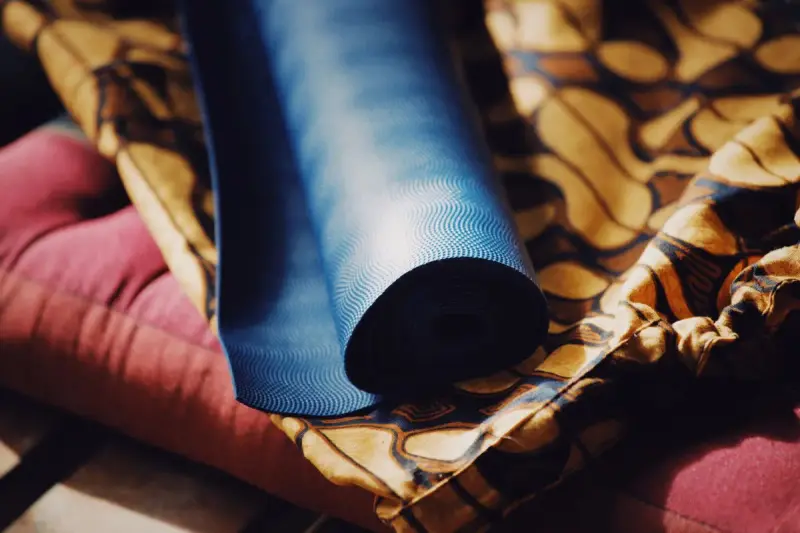 A rolled blue yoga mat resting on colorful patterned fabric