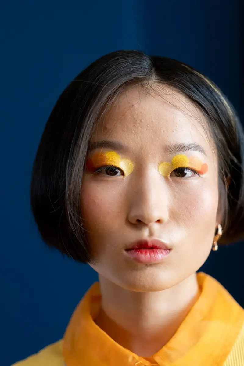 Woman with yellow and orange graphic eyeshadow on a deep blue background