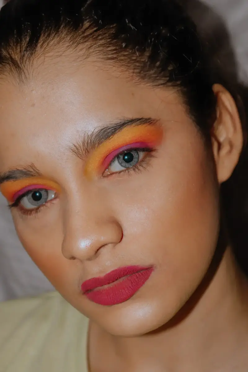 Close portrait of a woman with orange and pink eyeshadow and berry lipstick