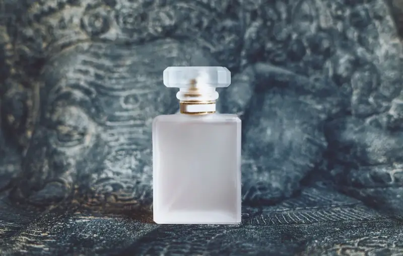 Square frosted perfume bottle with a gold collar on a dark textured background