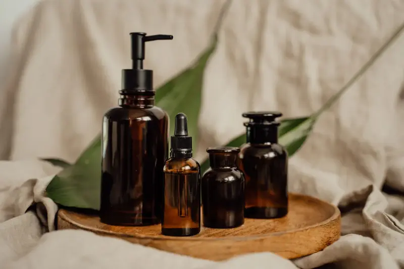 Amber glass skincare bottles arranged on a wooden tray with linen behind