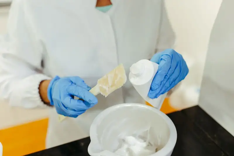 Gloved hands of a lab technician mixing a skincare cream sample