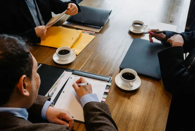 Business partners meeting at a wooden table with coffee and documents