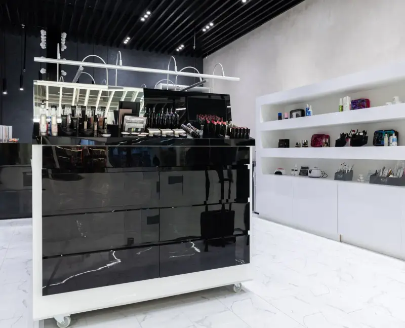 Glossy black cosmetics island with tester rows and white shelving behind