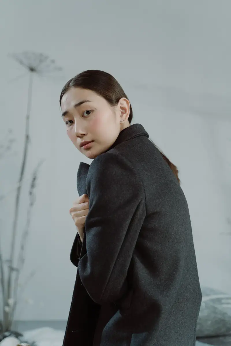 Woman in a charcoal wool coat looking over her shoulder in soft winter light