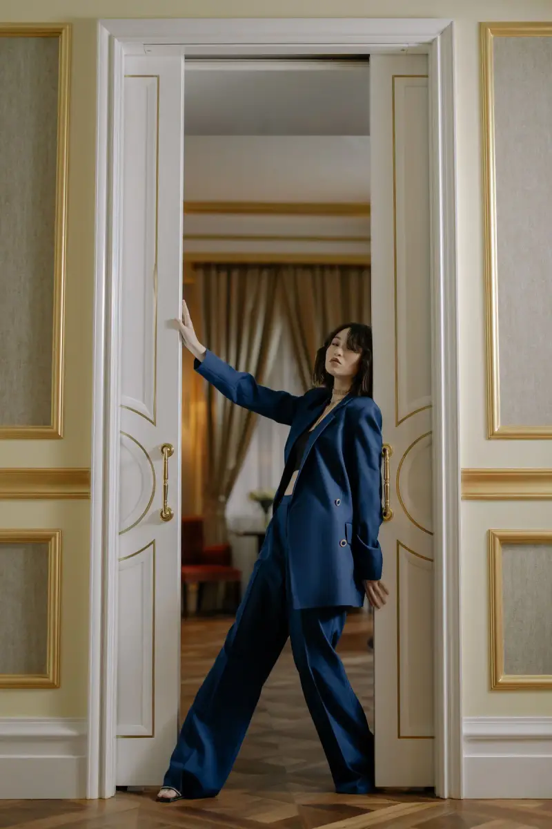 Woman in a navy oversized suit leaning in a tall white paneled doorway