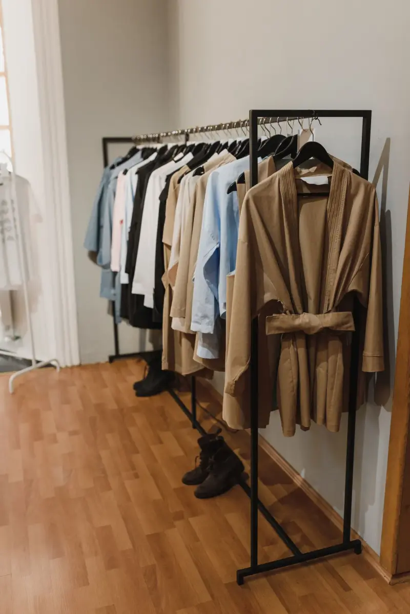 Beige belted trench coat hanging among light garments on a rack
