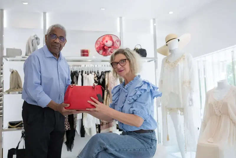 Two shoppers looking at a red handbag in a bright boutique