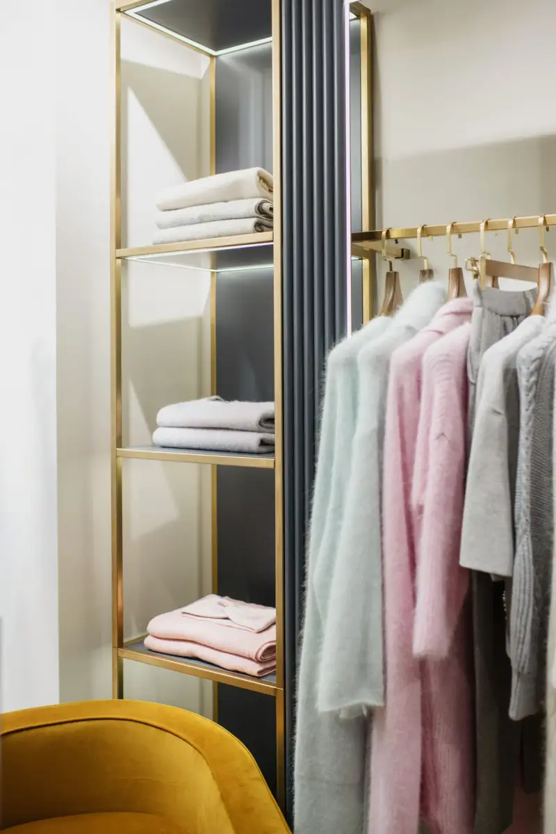 Pastel knitwear on a brass rail beside folded pieces on a shelf