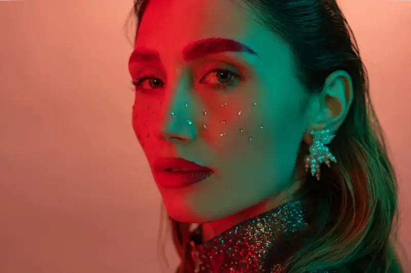 Woman in red and green gel light wearing a sculptural cluster earring and jeweled collar