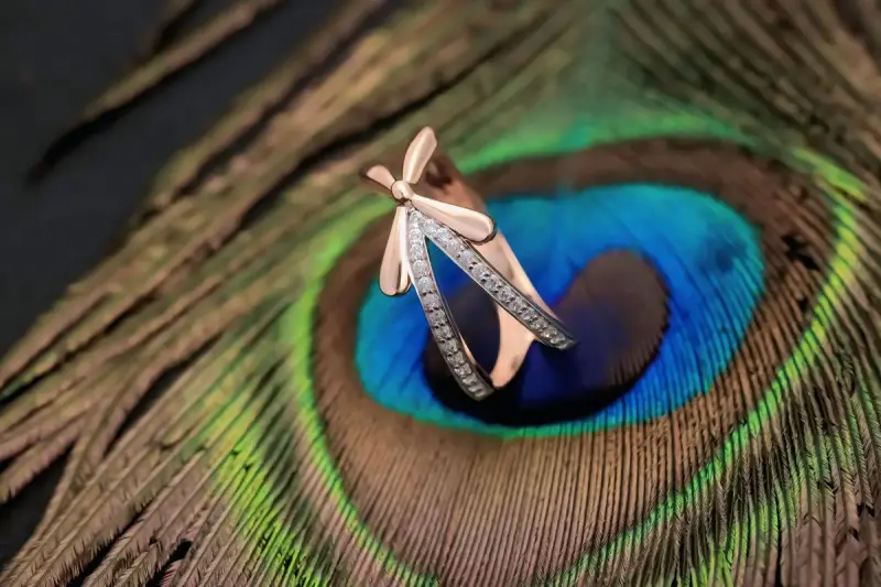 Rose gold ring with diamonds resting on a peacock feather
