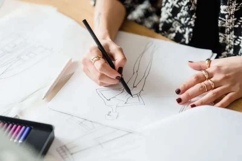 Designer wearing gold rings drawing a figure with pencil on paper