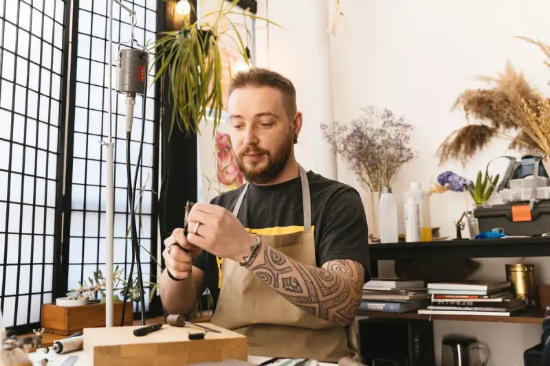 Jewelry artisan in an apron working in a sunlit studio full of tools and plants