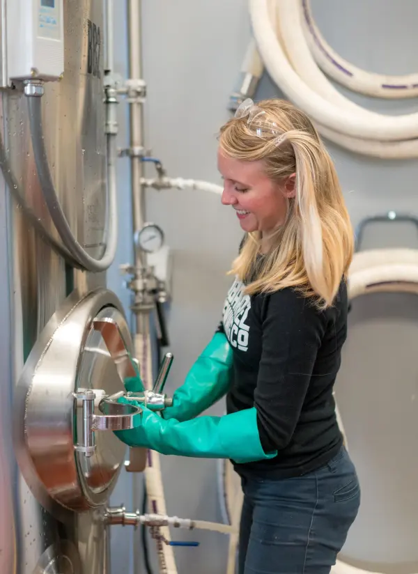 Female brewery professional operating equipment while wearing protective gloves