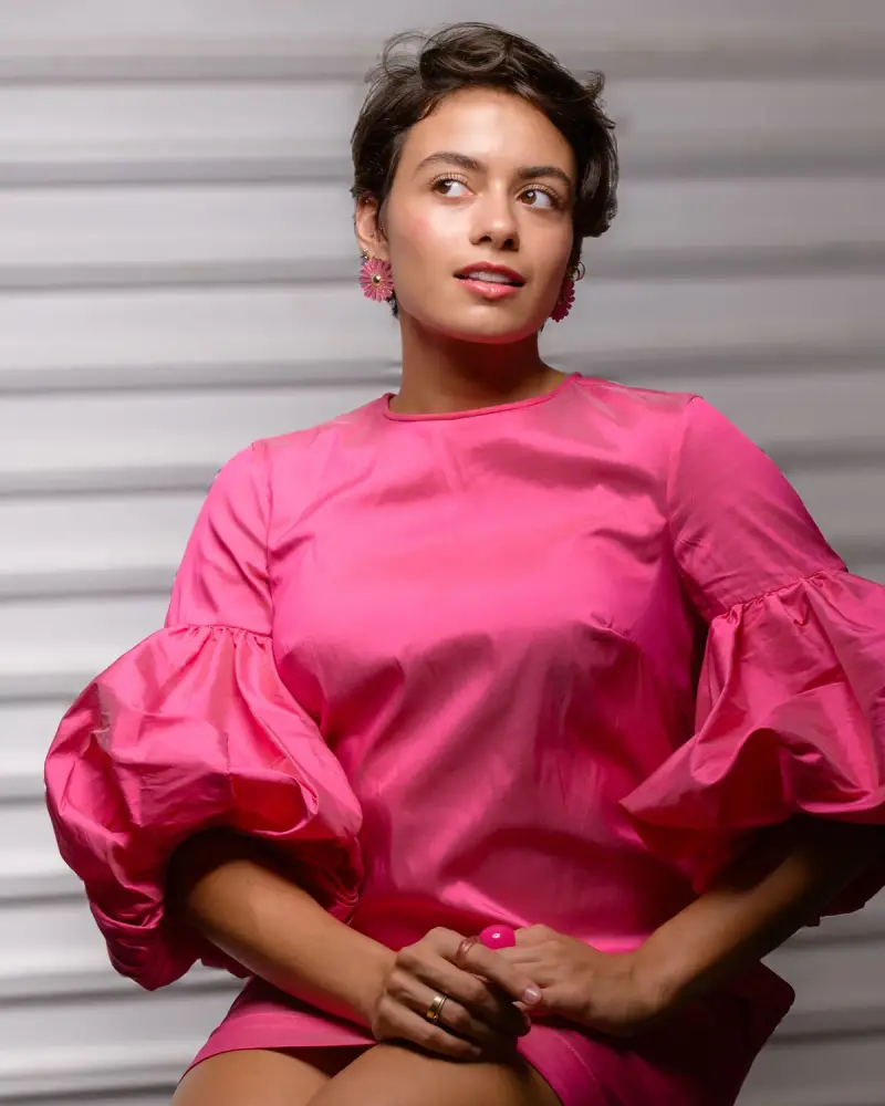 Woman in a fuchsia dress with dramatic puff sleeves and pink earrings, seated