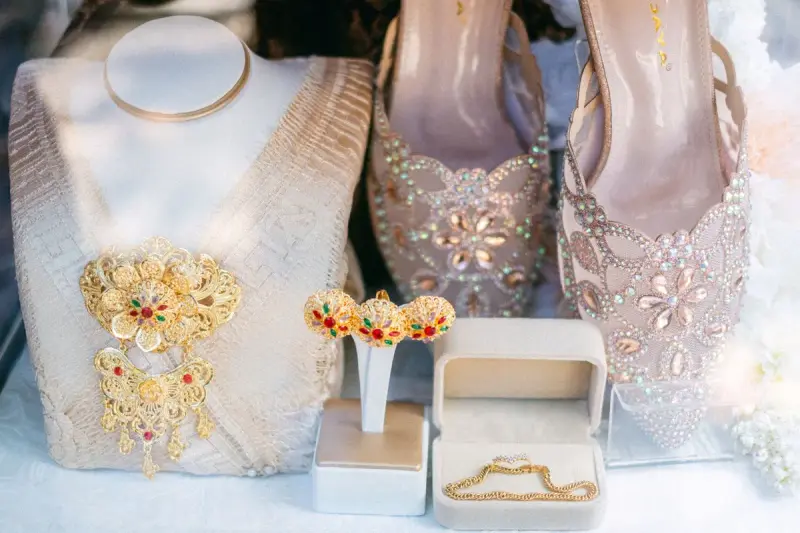 Gold necklace and earrings displayed beside embellished pink heels on a white stand