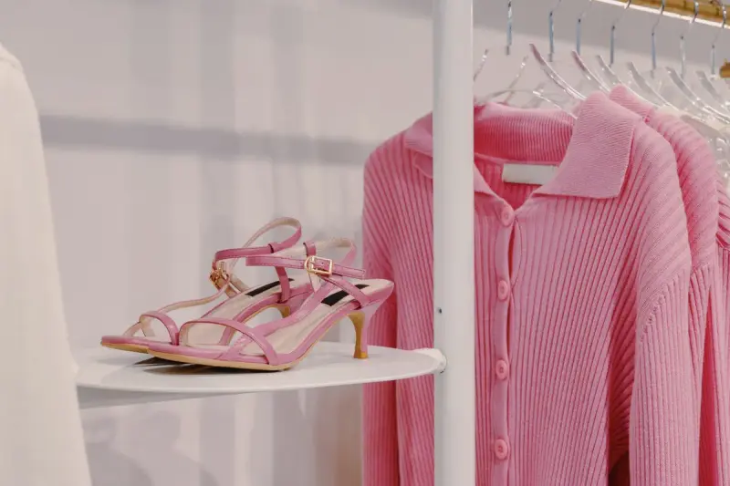 Pink strappy sandals on a round shelf next to a pink knit cardigan on a hanger