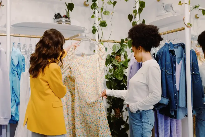 Two women looking through floral and pastel dresses on a rail in a bright boutique