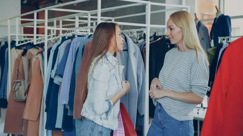 Two women talking among racks of shirts and jackets in a clothing store