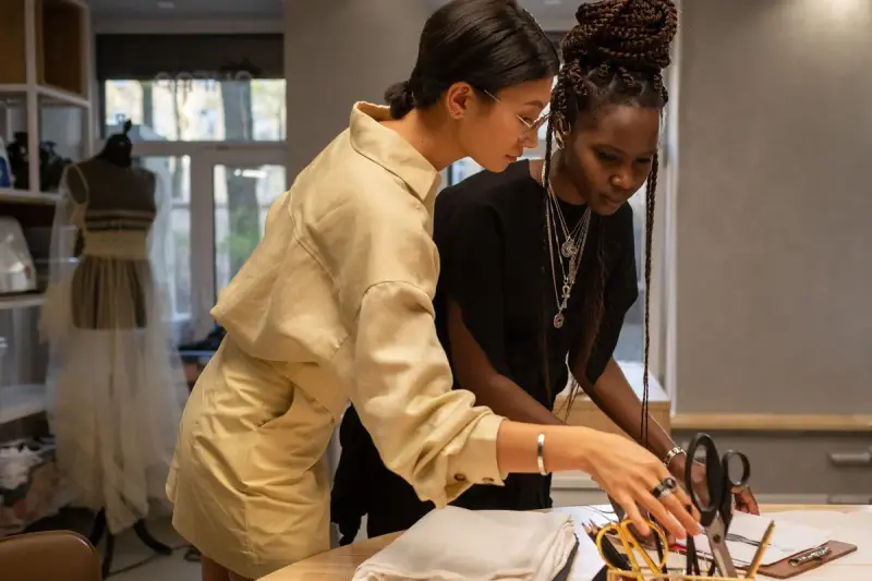 Two designers arranging fabric and tools on a work table in a sewing atelier
