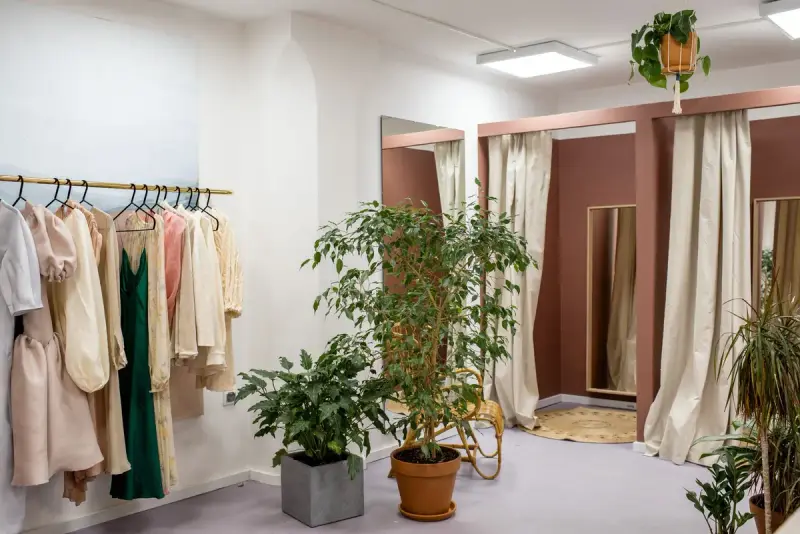 Boutique corner with dresses on a brass rail, plants and curtained fitting rooms