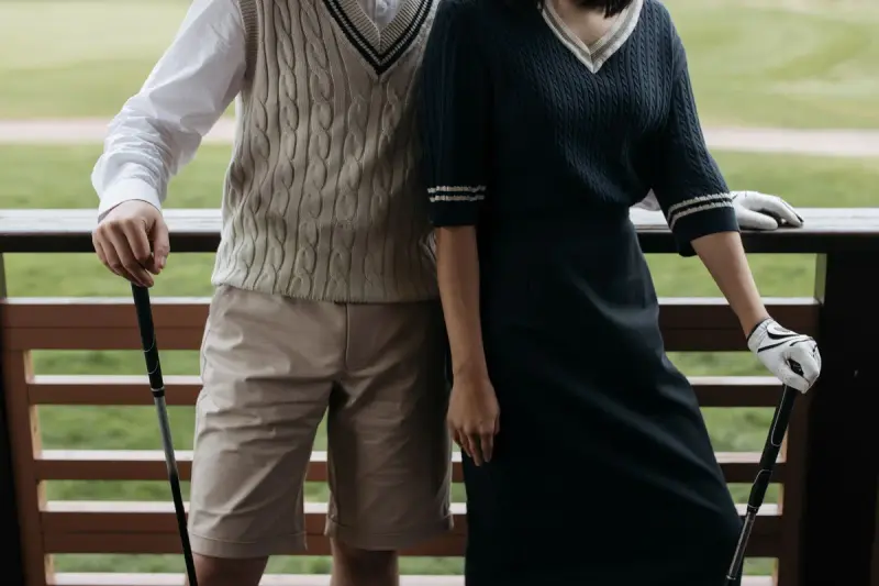 Golf couple in a cable-knit vest and a navy knit dress leaning on a clubhouse rail