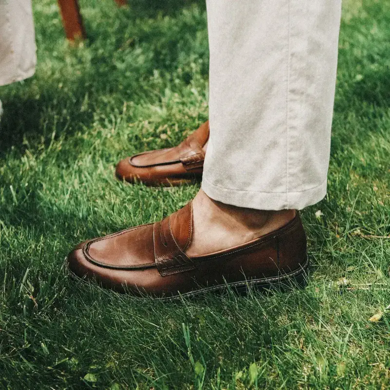 Brown leather loafers with stone-colored trousers on green grass