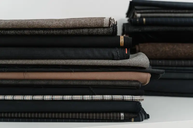 Stacks of folded suiting and coating fabrics in charcoal, brown and herringbone