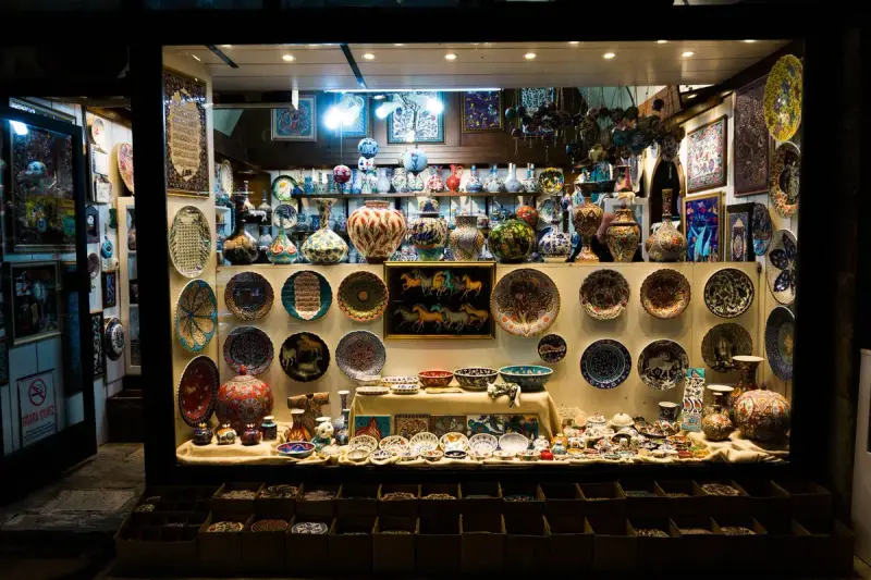 Lit shop window packed with painted ceramic plates, bowls and vases at night
