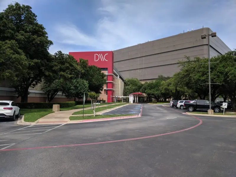 Dallas Market Center Trade Mart building with its red sign above a tree-lined drive