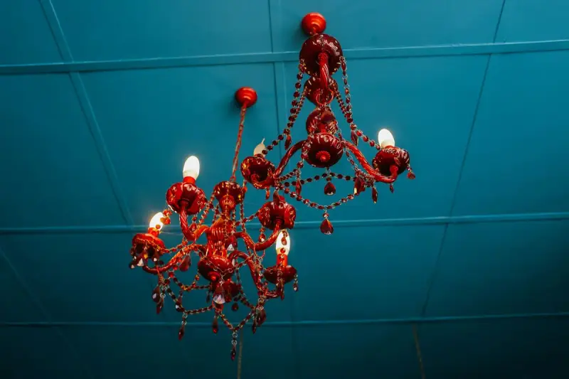 Red crystal chandelier with candle bulbs hanging against a teal ceiling