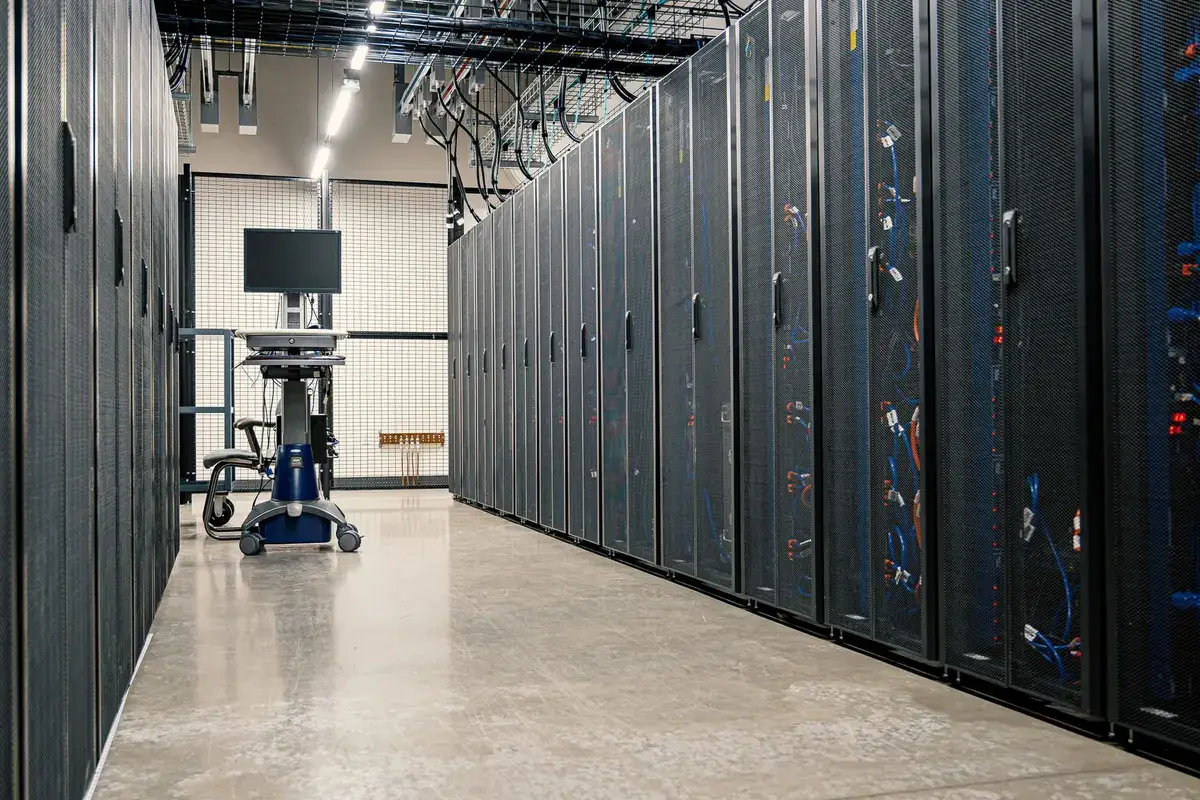 Long aisle of black server cabinets with overhead cable trays and a mobile workstation