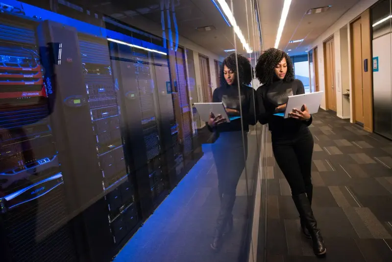 Woman engineer working on a laptop beside a glass wall of lit server racks