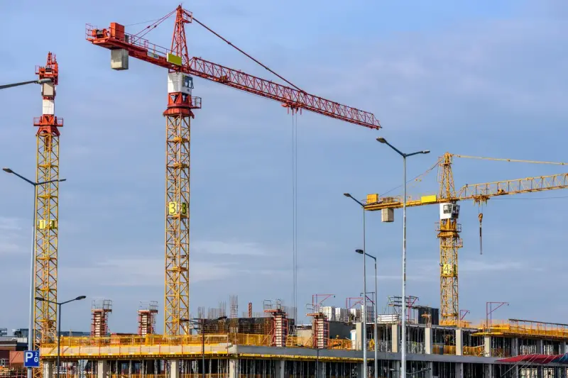 Several yellow and red tower cranes working over a large construction site