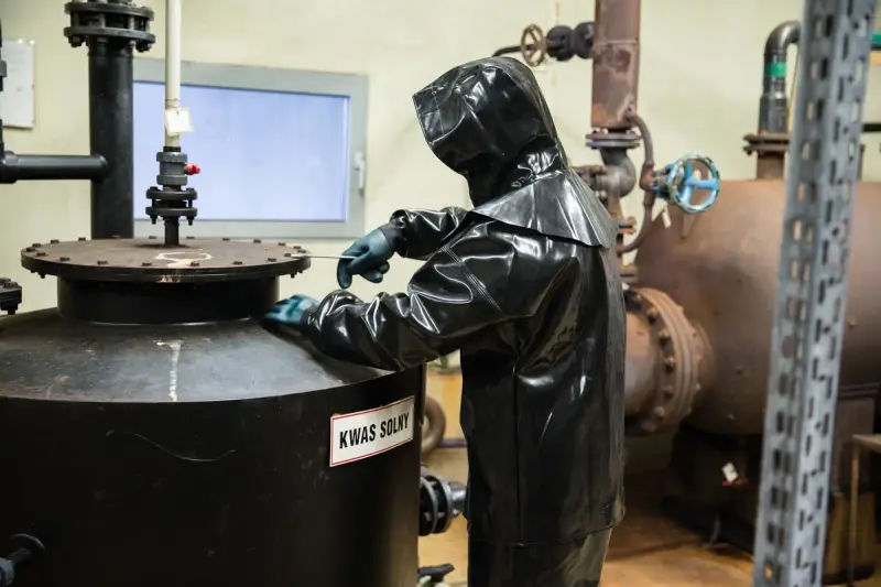 Worker in a chemical protection suit checks a storage tank in a plant room