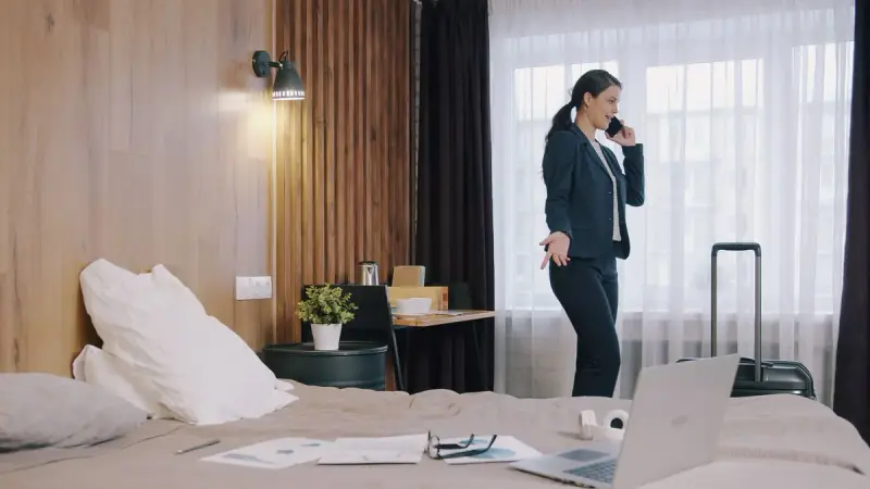 Businesswoman on a phone call in a hotel room with a laptop and papers on the bed