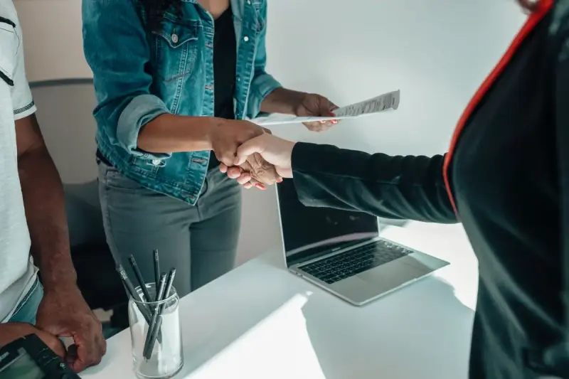Two people shaking hands over a desk during a business meeting